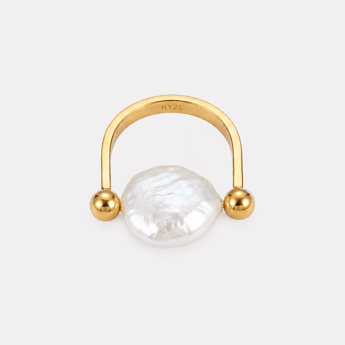 A gold hoop ring with a large, irregular white baroque pearl centered in front, set against a light gray background. The inner band of the gold ring is engraved with the brand name 'HYZL'.