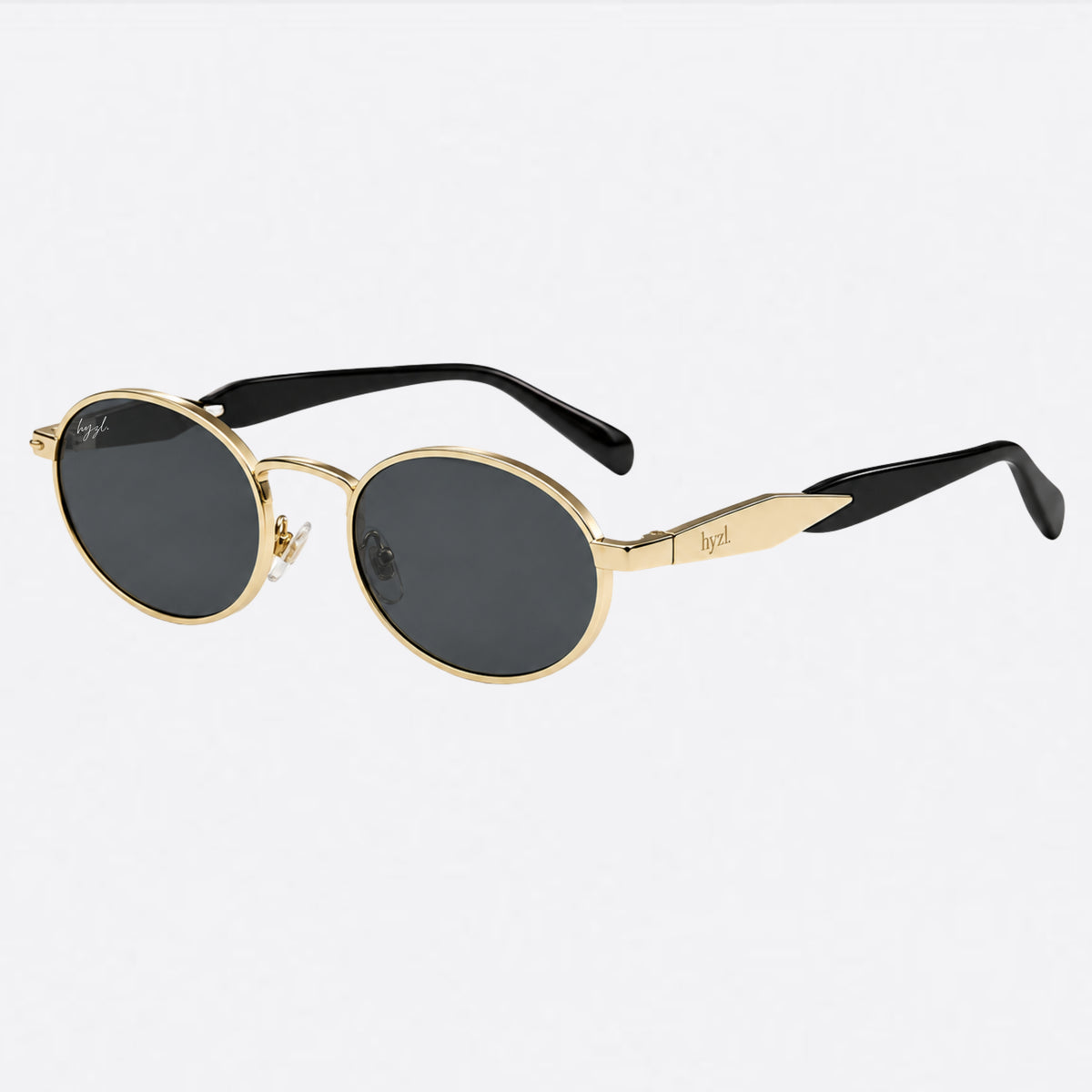 Oval sunglasses with a gold metal frame, dark lenses, and black temple tips, shown against a light gray background.