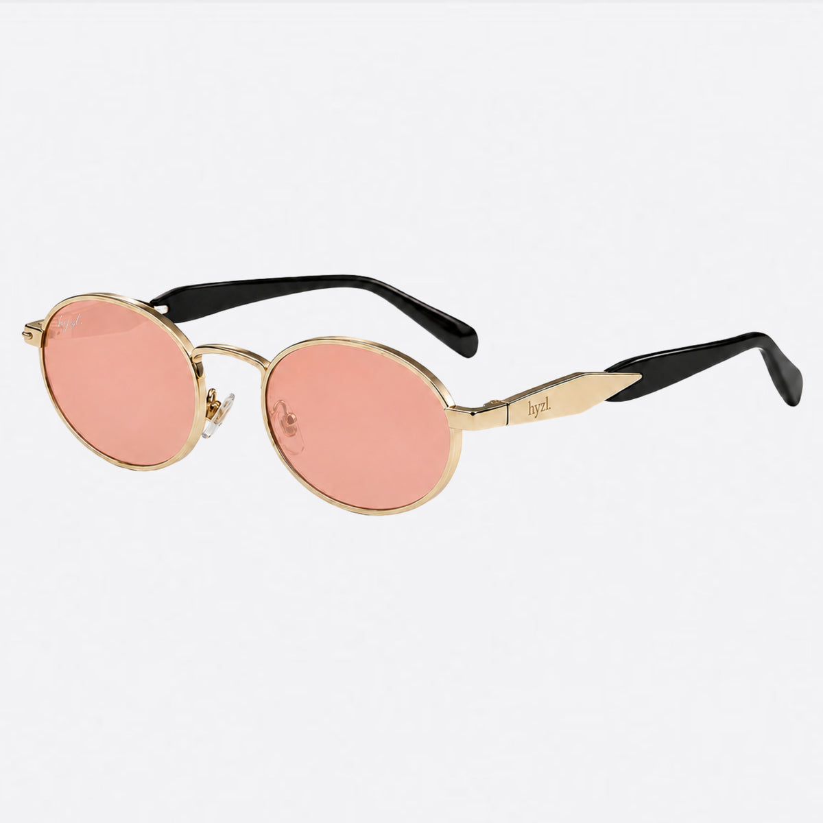 Oval sunglasses with gold-tone metal frames, pink-tinted lenses, and black temples, shown on a light gray background.