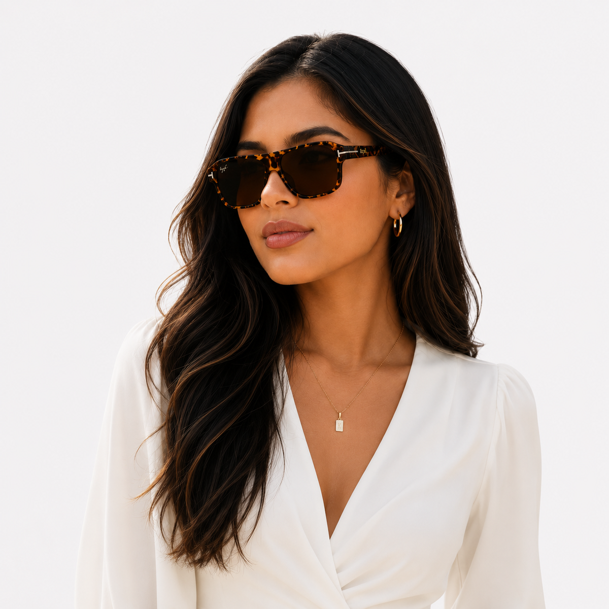 A woman with long dark wavy hair wearing tortoiseshell sunglasses and a white V-neck top, photographed against a clean white background.
