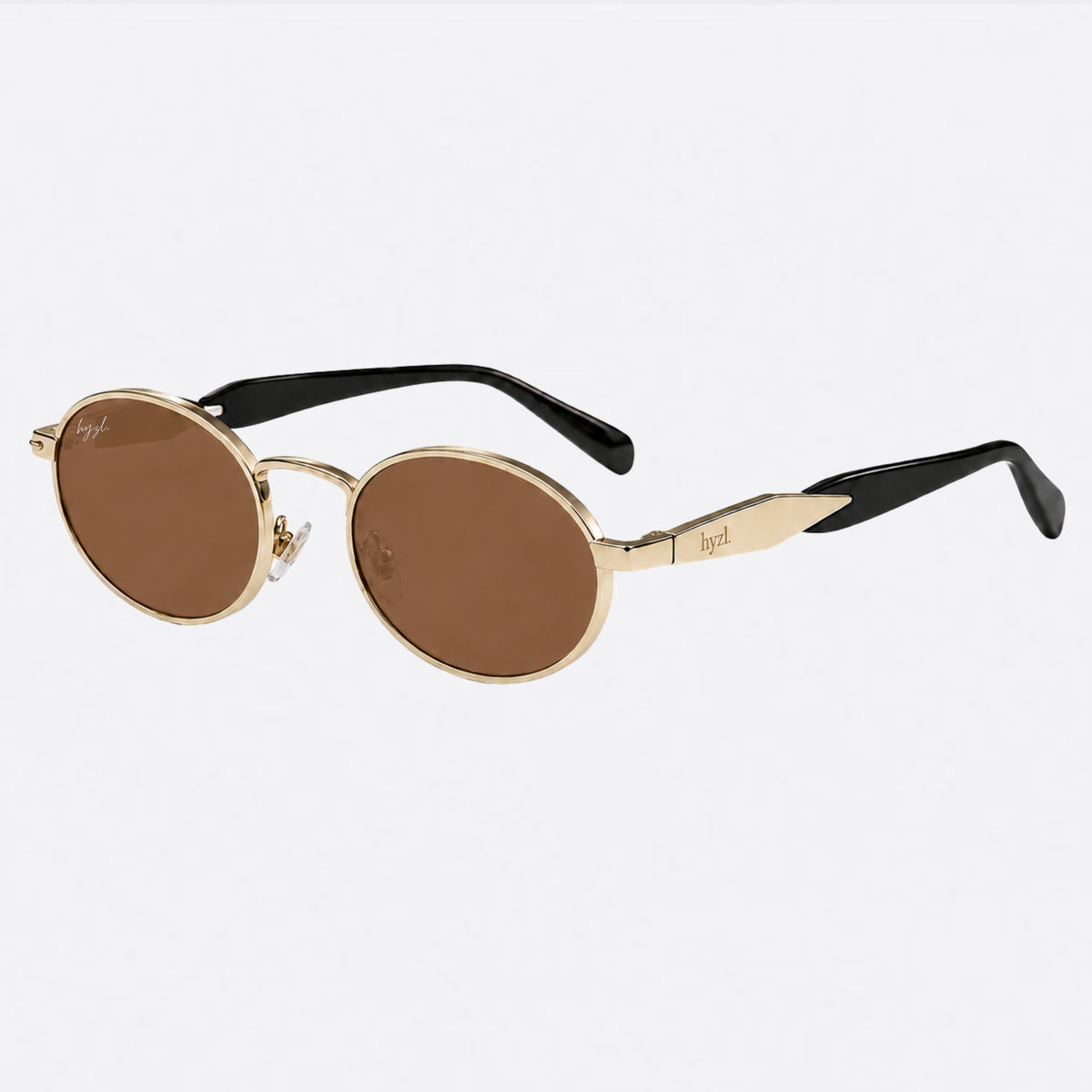 Oval sunglasses with gold metal frames, brown lenses, and black temples, shown on a light gray background.