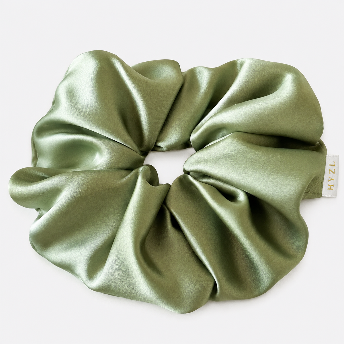 An olive green satin hair scrunchie with a small white brand tag reading 'HYZL', shown on a clean white background.