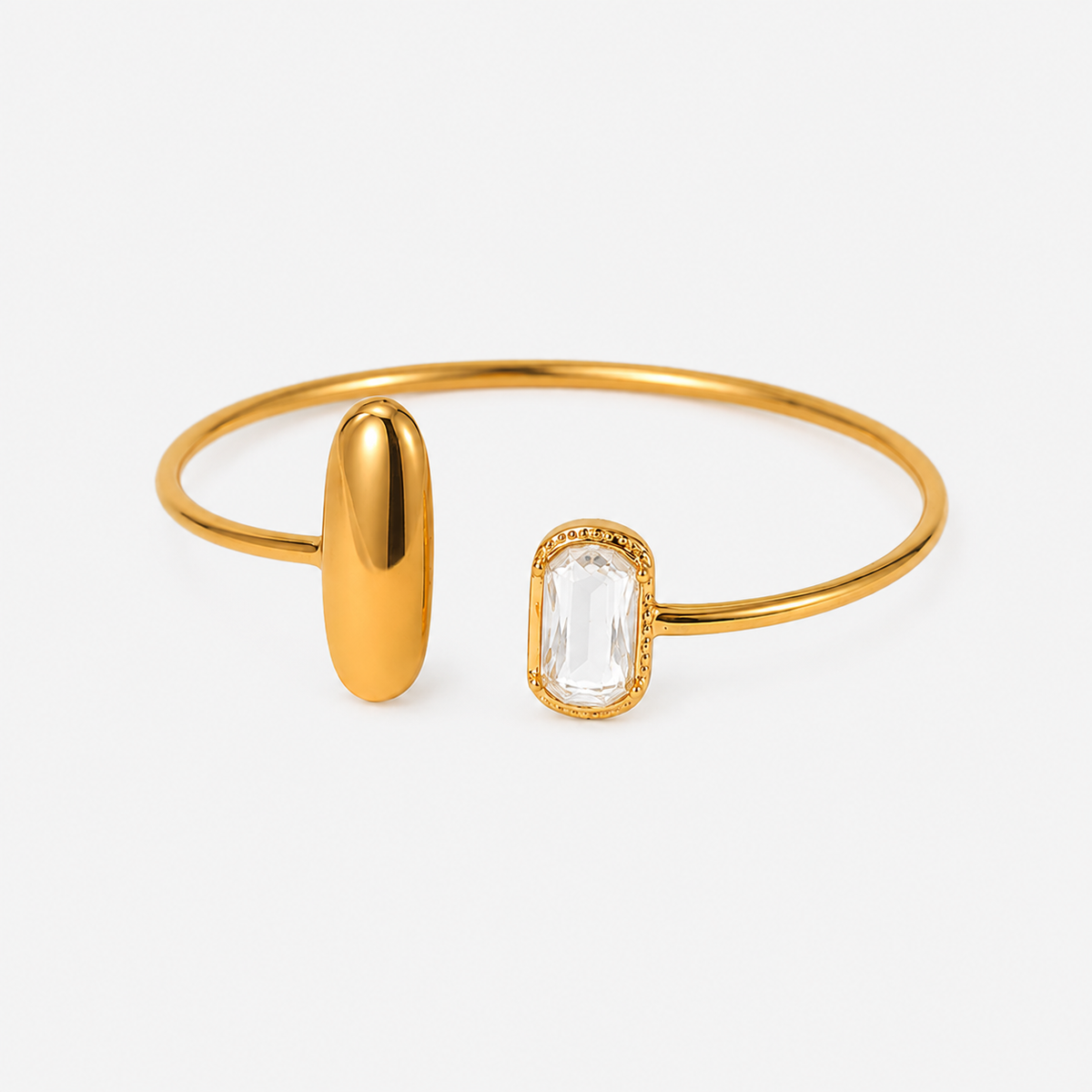 Gold bangle bracelet with a polished oval gold spacer and a clear rectangular baguette gemstone in a gold bezel setting, shown on a light gray background.