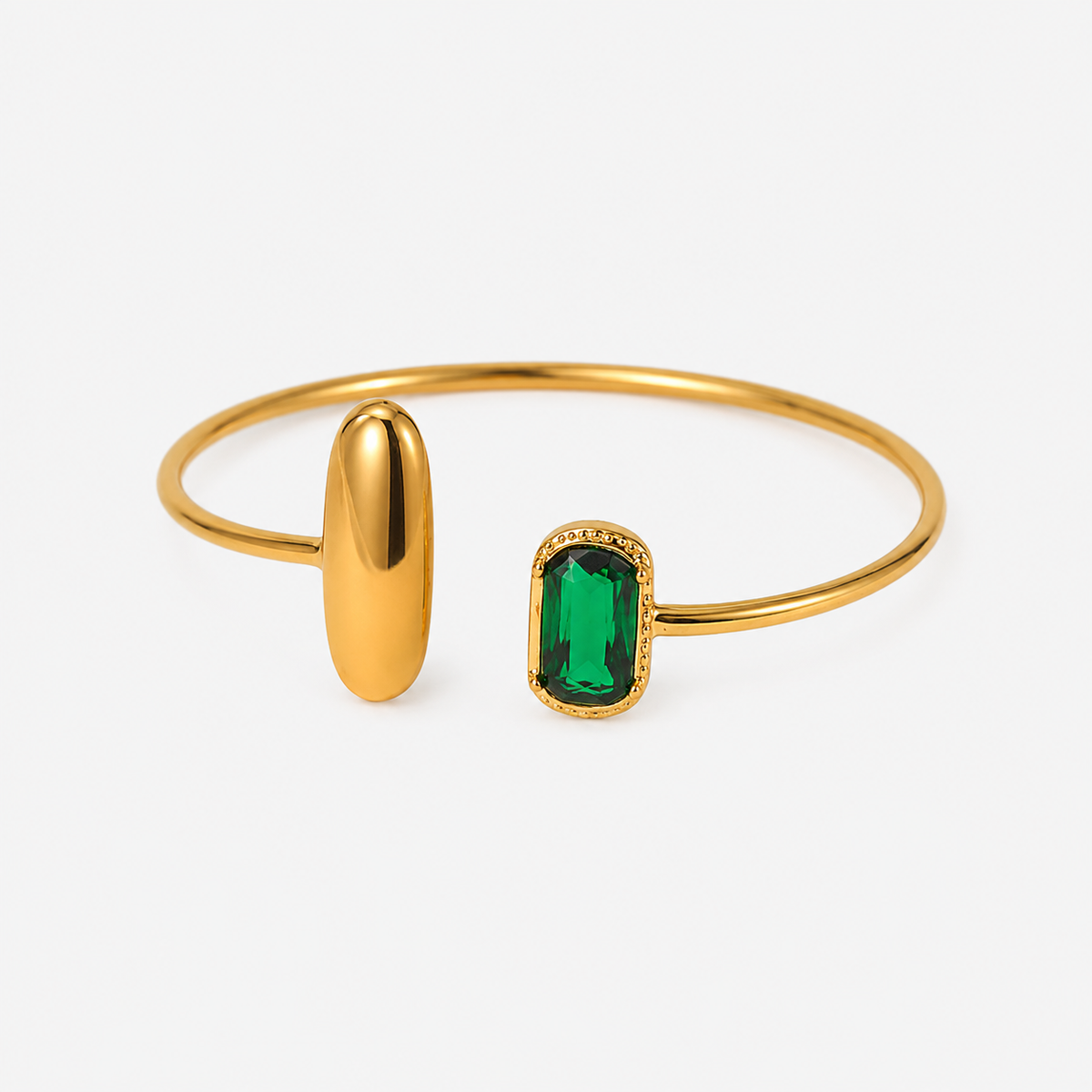 Gold bangle bracelet featuring a polished oval gold end and a rectangular emerald-cut green gemstone end with a delicate gold border, shown on a light gray background.