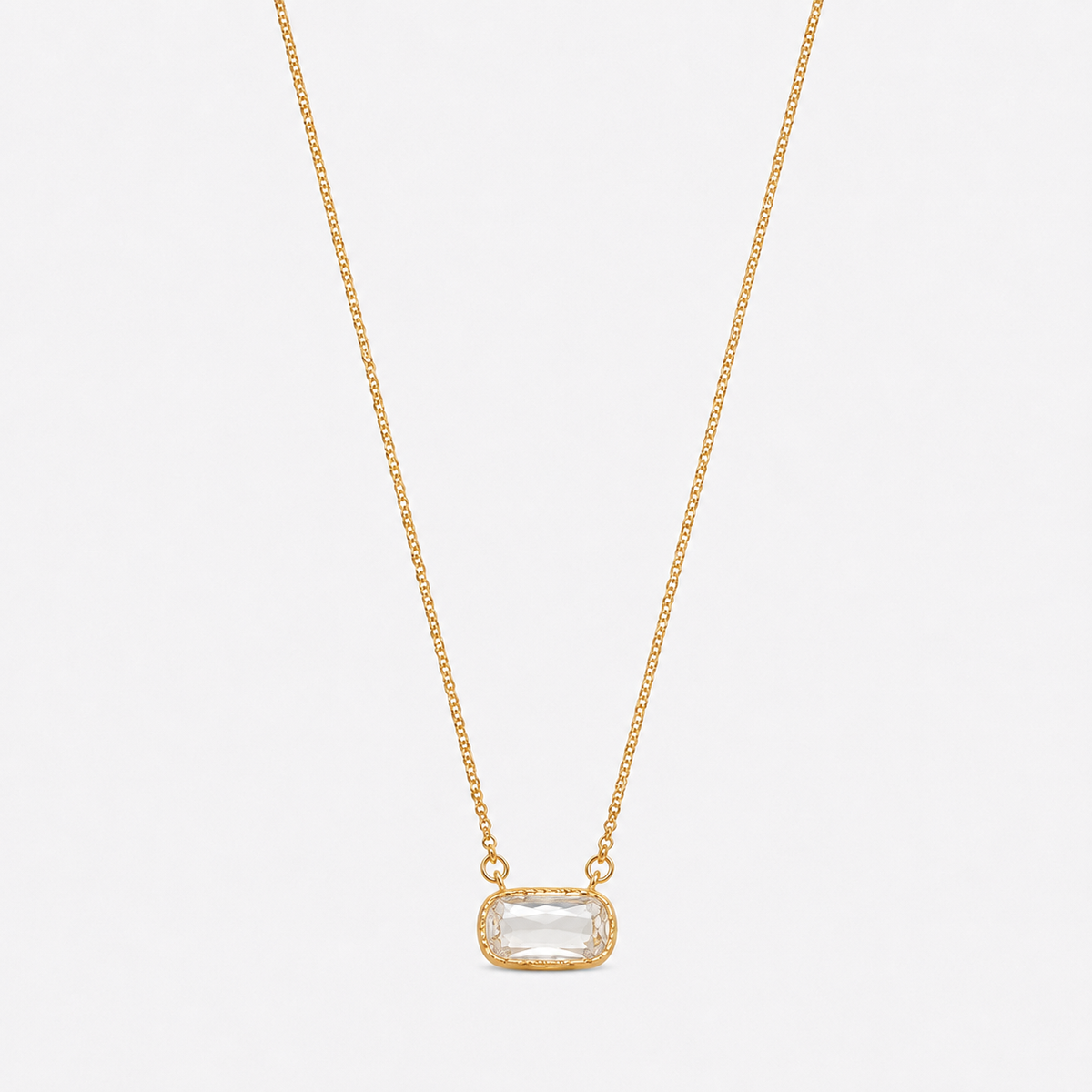 A delicate gold chain necklace with a small rectangular bezel-set clear gemstone pendant, displayed against a light gray background.