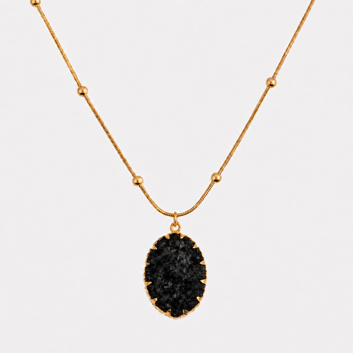 A gold chain necklace with a black druzy stone pendant, displayed against a light gray background.