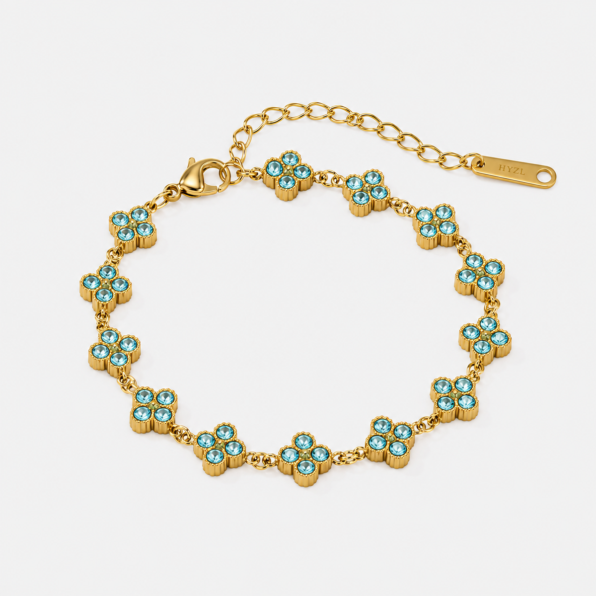 A gold-tone bracelet with repeating flower motifs set with light blue rhinestones, shown on a clean white background. A gold tag is attached to the extender chain.