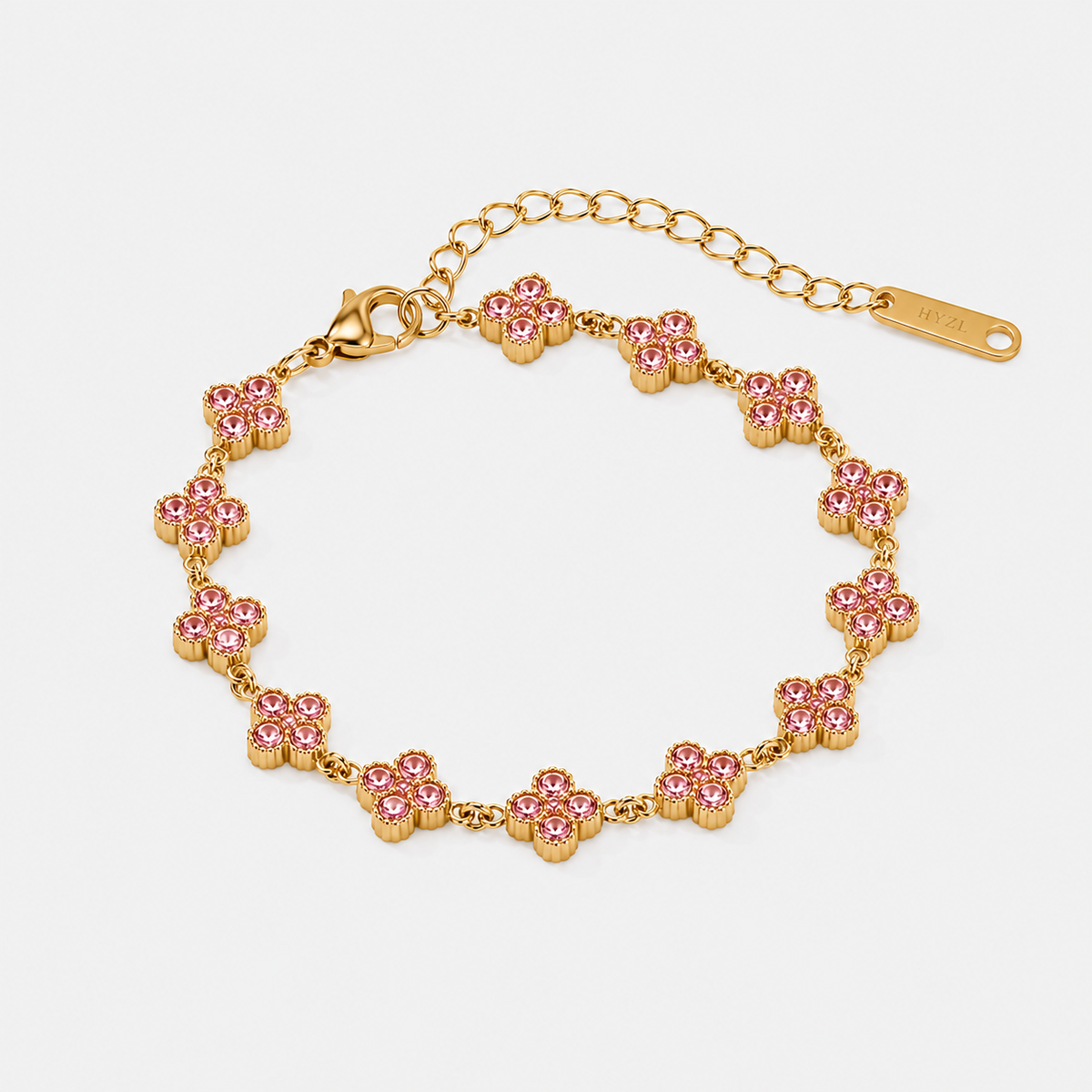 A gold-tone bracelet featuring a series of small flower motifs paved with pink rhinestones, complete with an adjustable link chain and clasp, shown on a light gray background.