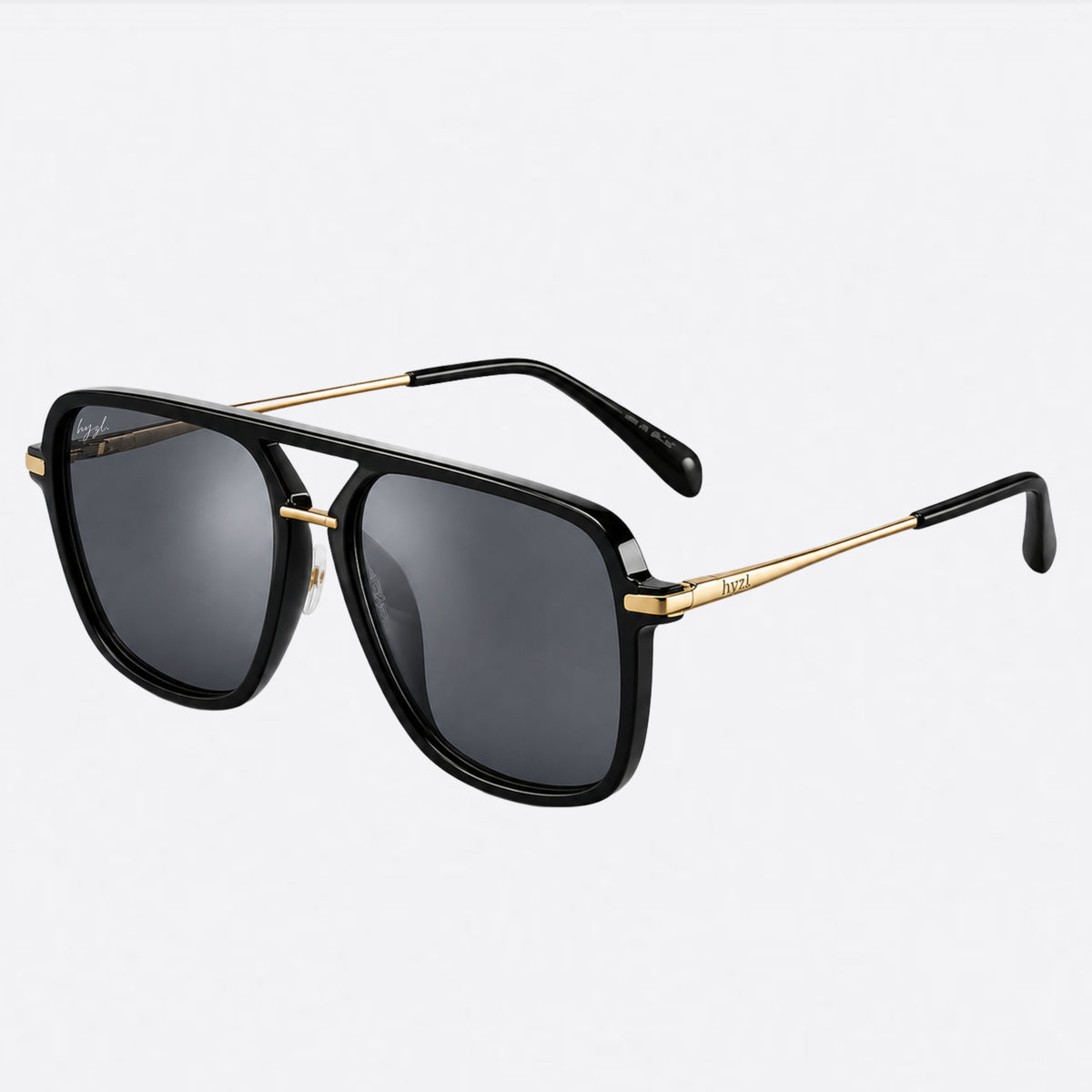 A pair of aviator-style sunglasses with a glossy black frame, dark gray lenses, and gold metal arms, shown on a light gray background.